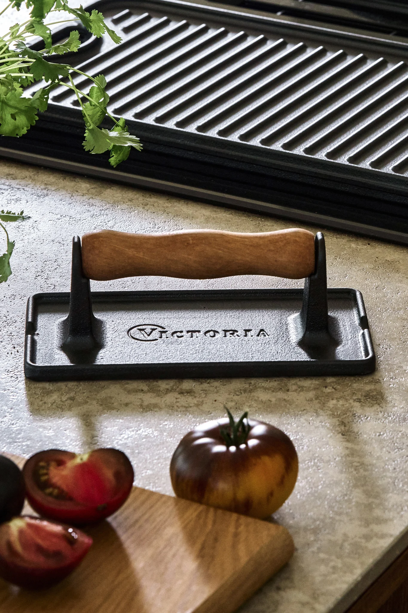 En støpejerns-kjøttpresse står på kjøkkenbenken ved siden av tomater og en grillplate.