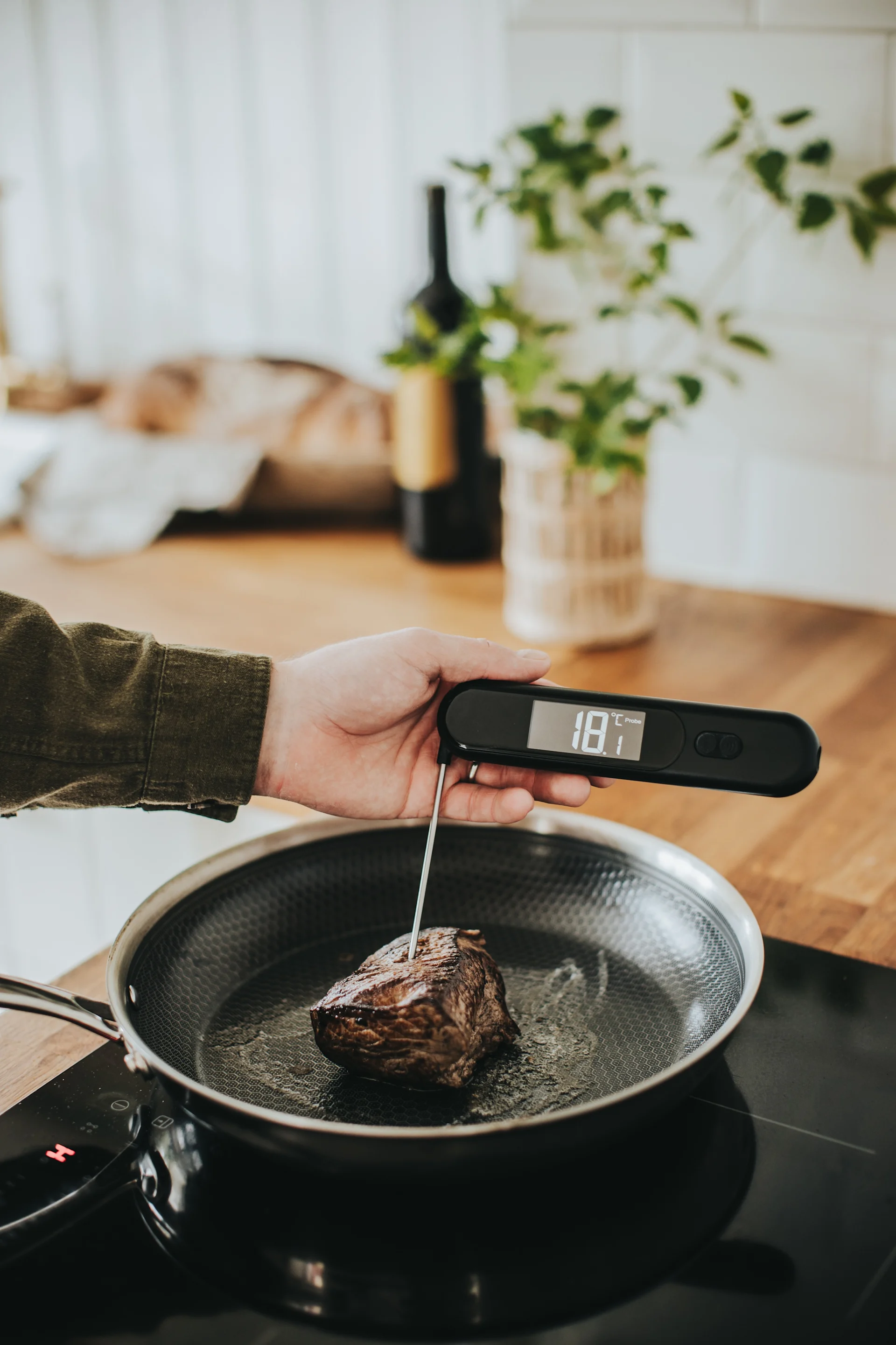 Hånd sjekker kjøttemperatur med et digitalt termometer i en stekepanne.