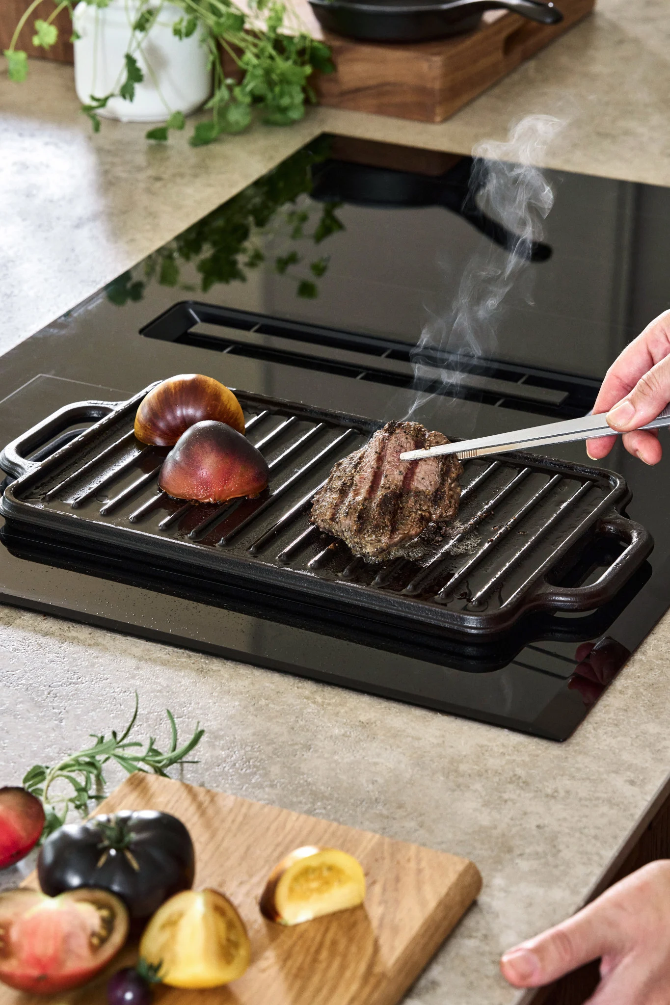 En støpejernsplate på en induksjonskomfyr med et par tomater og et stykke biff.