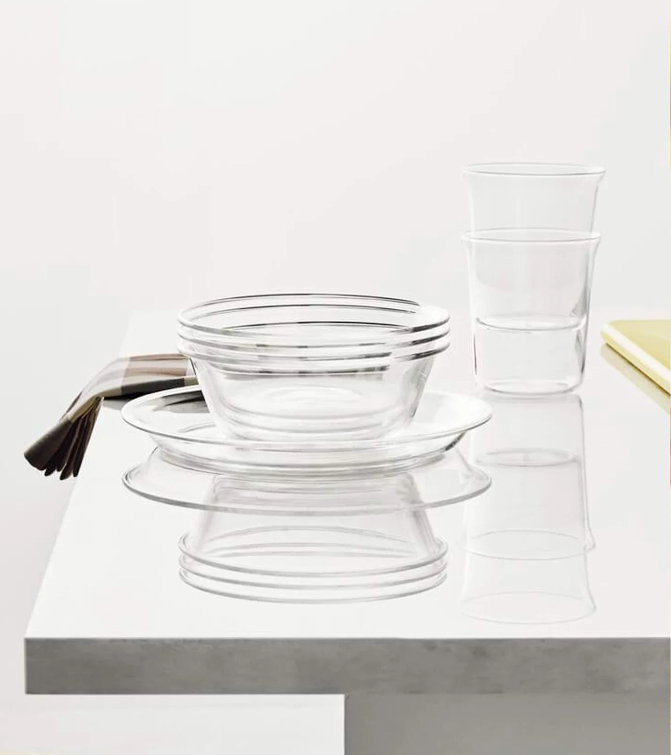 Klare glassboller, tallerkener og vannglass stablet på en hvit overflate med en stripet serviett.