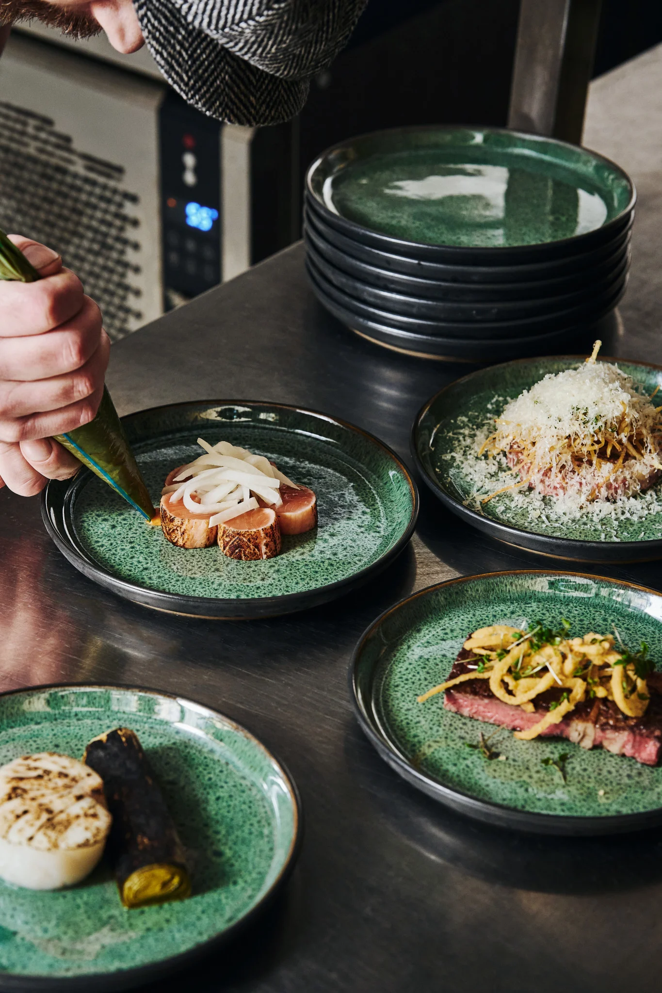 Hender sprøyter saus på en grønn tallerken på et profesjonelt kjøkken. Lær hvordan du anretter mat som en profesjonell med vår guide.
