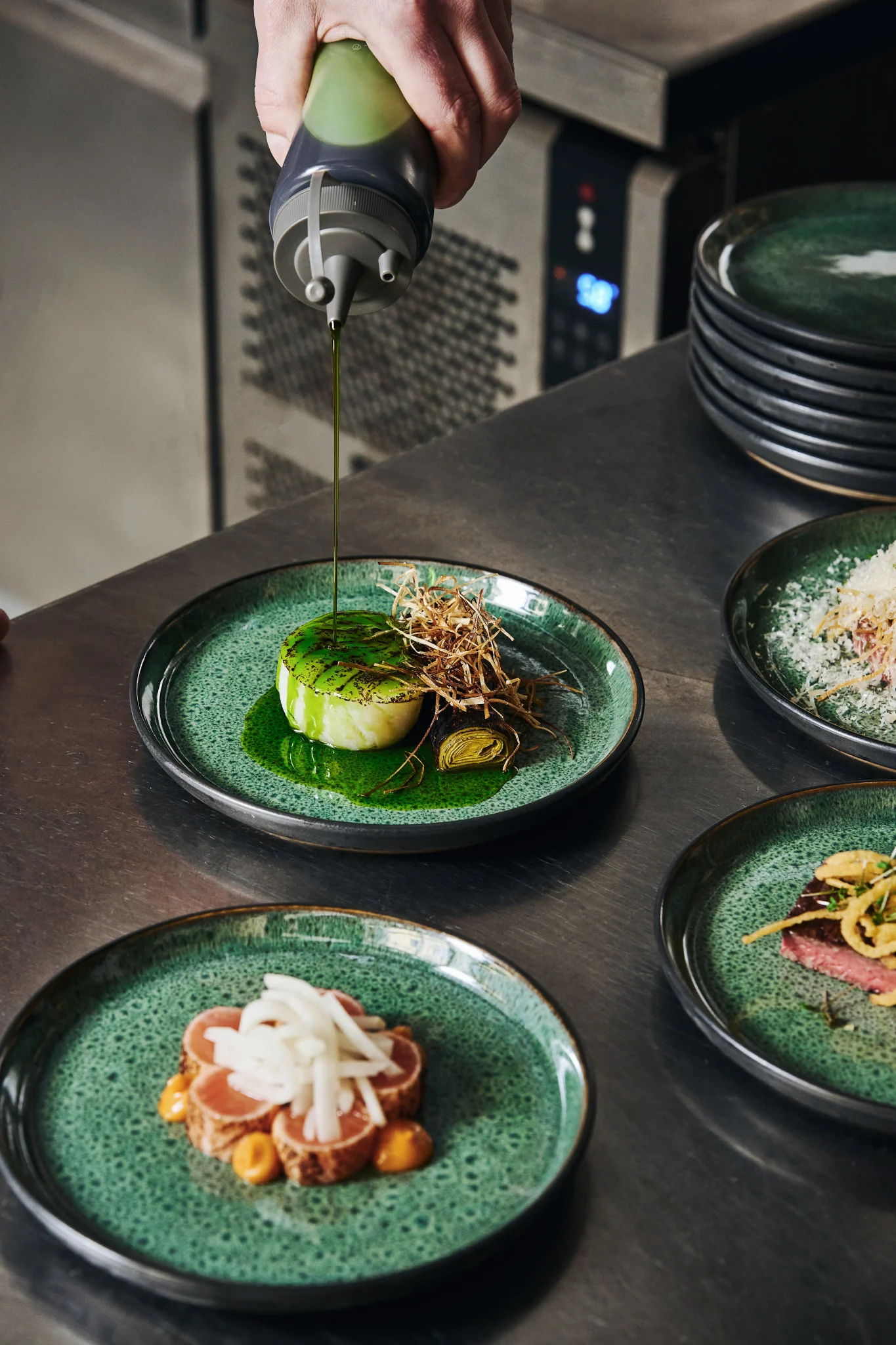 Riktig verktøy gjør det enklere å anrette som en profesjonell. Her ser du klemmeflasken Plate it i bruk til garnityr – med grønn olje som helles over en tallerken med mat.
