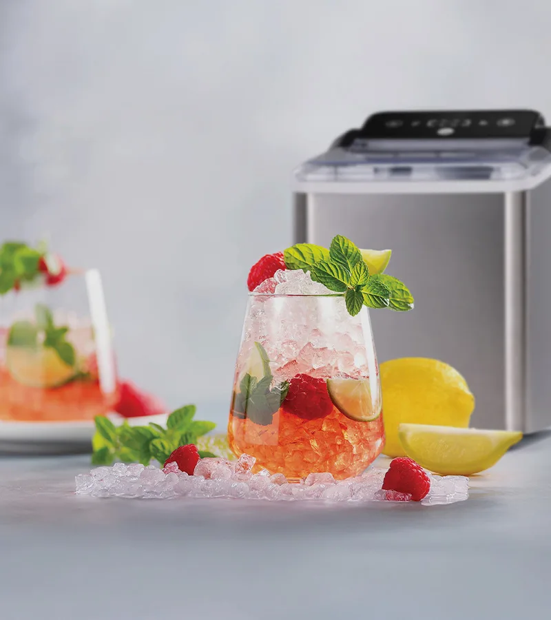 Forfriskende drink med knust is, bringebær, lime, mynte, en ismaskin og spredt is med sitron.