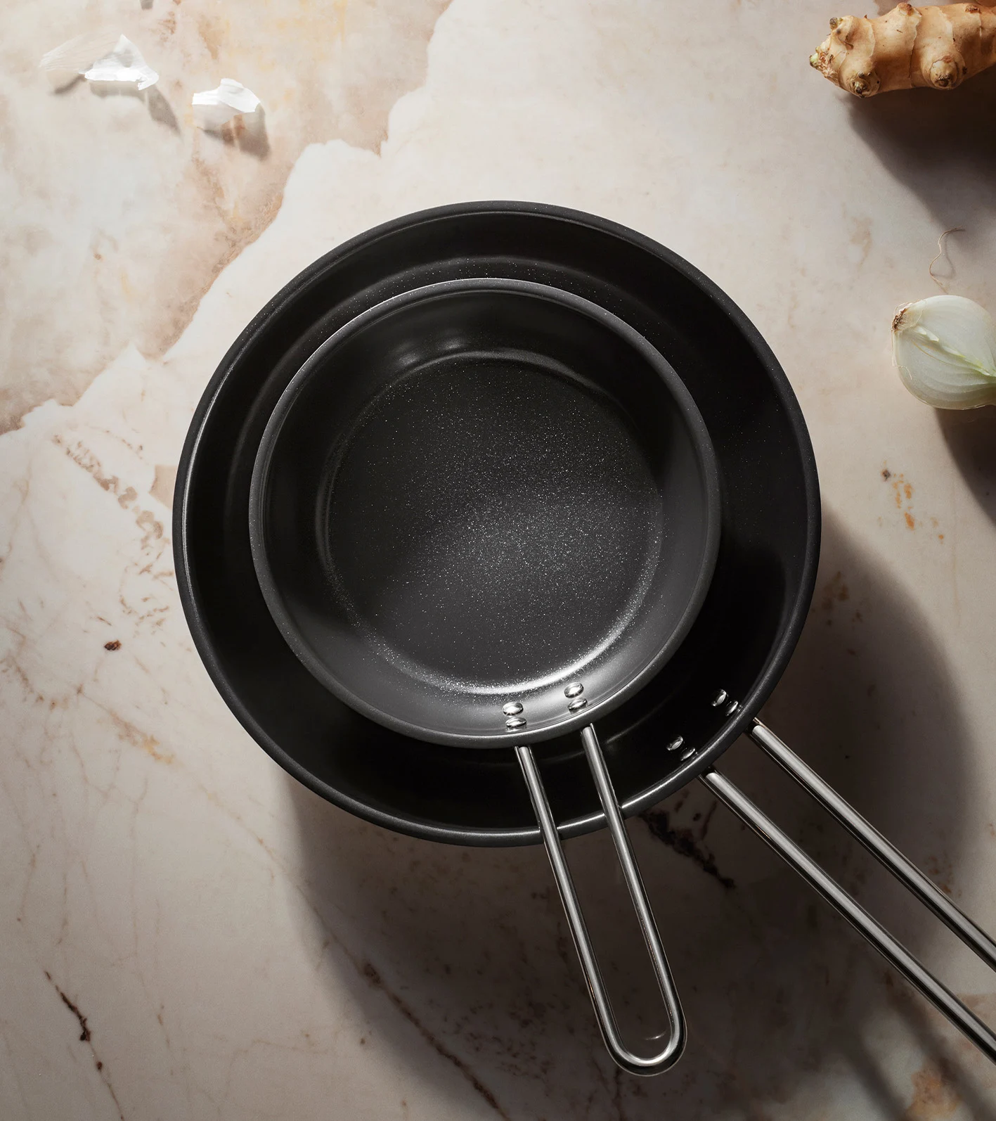 To sorte non-stick stekepanner, den ene inni den andre, på en marmoroverflate.