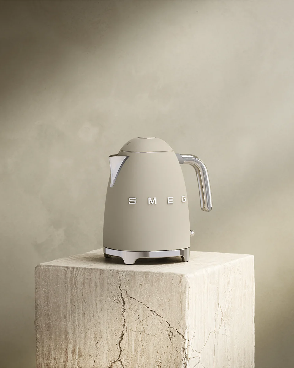 Beige Smeg vannkoker med kromdetaljer på en teksturert steinblokk.