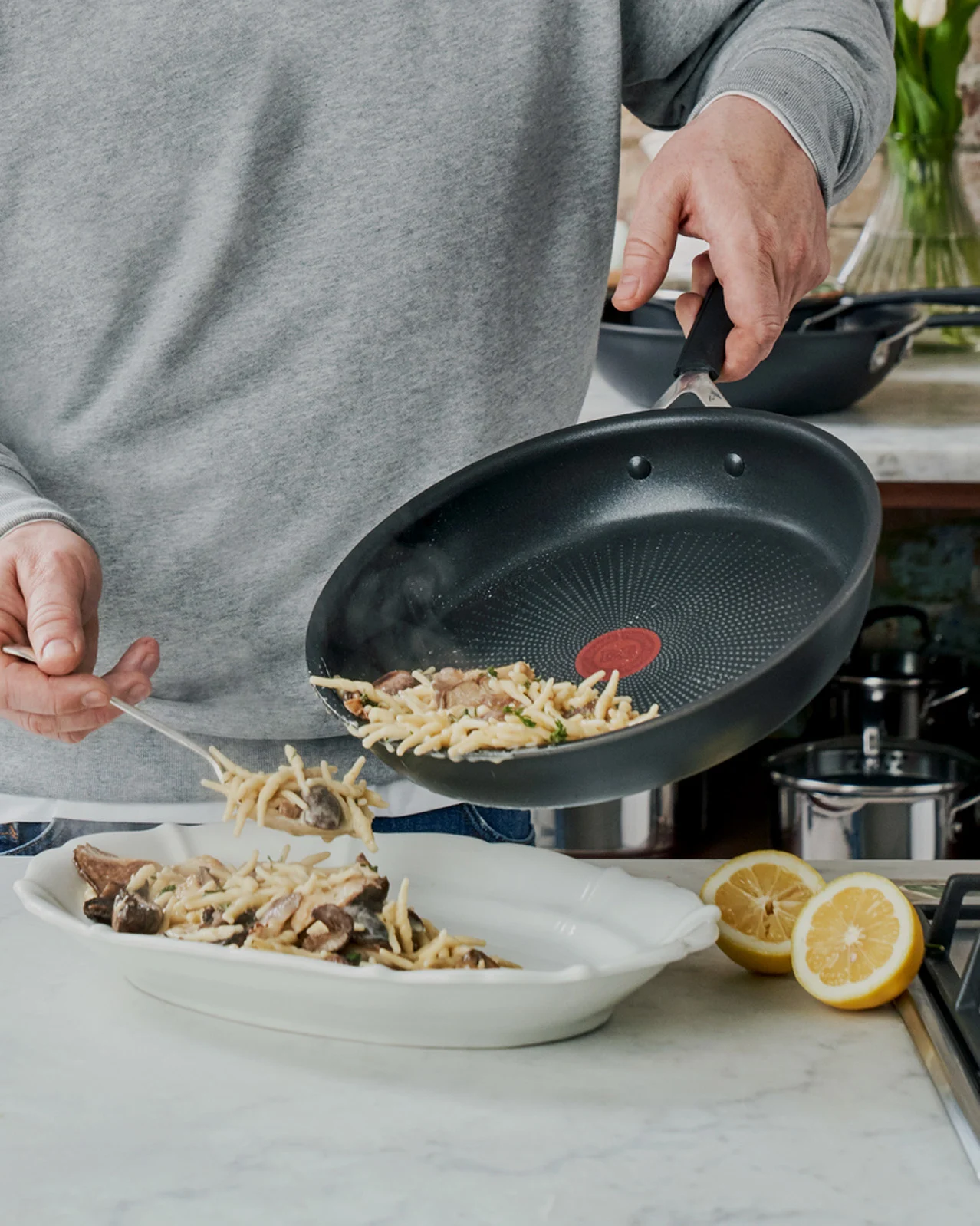 Person serverer pasta med sopp fra en stekepanne i en serveringsskål.